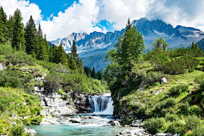 Scenic view of river and waterfall amidst trees against the sky