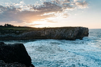 Rocks in sea against sky during sunset