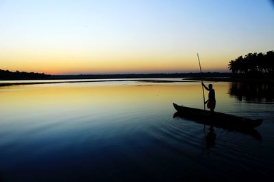 Silhouette man on boat in lake against sky during sunset