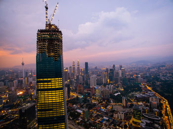 Illuminated buildings in city against cloudy sky