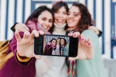 Happy women friends using mobile phone in front of colorful houses.costa nova, aveiro, portugal