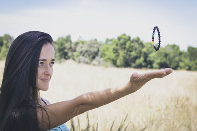 Portrait of smiling young woman against sky while levitating bracelet. 