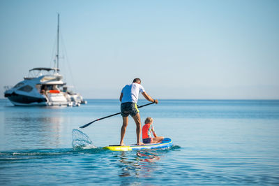 Rear view of man surfing in sea against clear sky