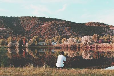 Rear view of man crouching by pond during autumn