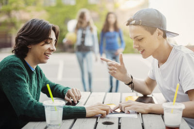 Happy male teenagers using digital tablet at table outdoors