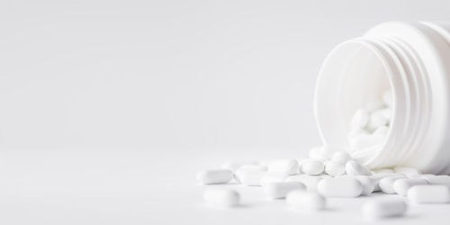 Close-up of pills spilling from bottle against white background