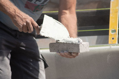 Close up of the hands of a bricklayer applying cement mortar to a brick