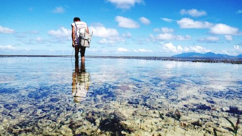 Low angle view of man with basket in sea against cloudy sky during sunny day