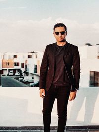 Portrait of young man wearing sunglasses standing against sky