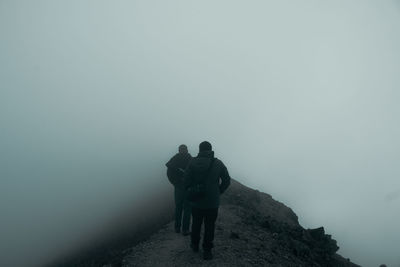 Rear view of man and woman walking on mountain against sky