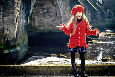 Portrait of smiling girl standing against pond during sunny day