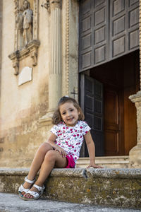 Portrait of a girl sitting against building