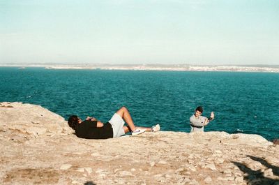 Couple sitting on beach by sea against sky