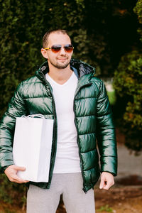 Mid adult man holding bag looking away while standing outdoors