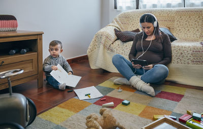 Mother using digital tablet while son holding book at home