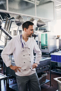 Thoughtful male chef standing with hands on hips in commercial kitchen