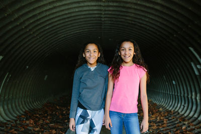 Twin tween girls smile for the camera in a tunnel