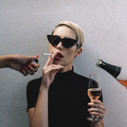 Close-up of woman standing by wall while cropped hand igniting cigarette