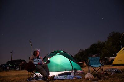 Man sitting in tent against sky at night