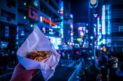 Cropped image of hand holding burger in city at night