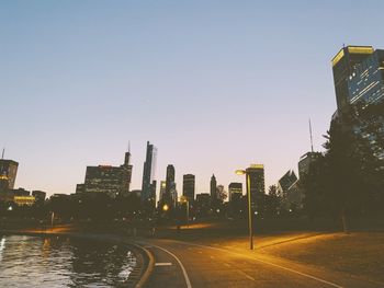 Road by buildings against clear sky in city