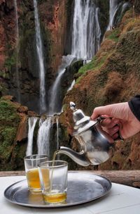 Cropped view of hand pouring tea in front of waterfall