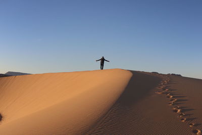 Man standing on sand dune in desert against sky