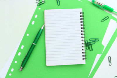 Directly above of spiral notepad on green file over white background