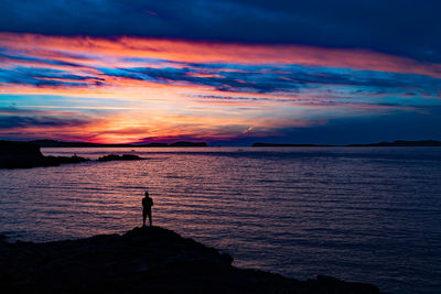 Silhouette man standing by sea against sky during sunset