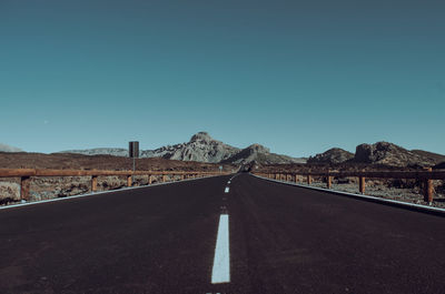 Road leading towards mountain against clear sky