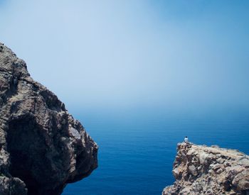 Rock formation by sea against clear blue sky