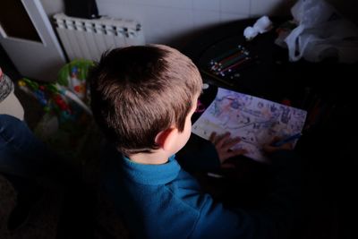 Rear view of boy using mobile phone at home