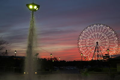 Fountain against illuminated ferris wheel at dusk
