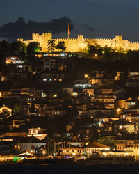 High angle view of illuminated city by sea against sky at night