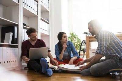 Three creative business people sitting on the floor discussing