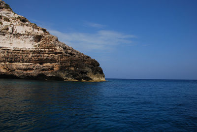 Rock formations by sea against blue sky