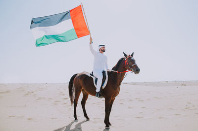 Full length of person riding horse on beach against sky