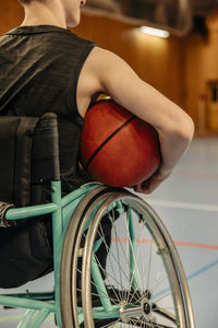 Rear view of girl with disability sitting on wheelchair while holding basketball at sports court