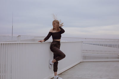 Full length of woman standing on railing against sky