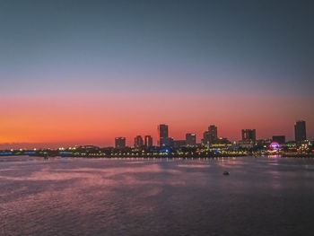 Illuminated buildings in city against sky at sunset