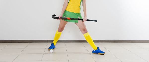 Low section of woman with hockey stick on tiled floor