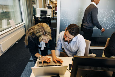 Businesswoman assisting male colleague over laptop in coworking office