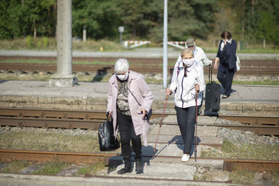 A group of senior travelers with masks on their faces cross the railway tracks