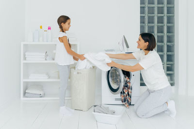 Mother with daughter washing clothes in machine at home