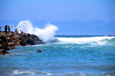Scenic view of waves splashing on rocks against blue sky