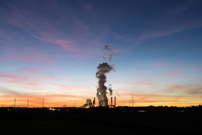 Smoke emitting from factory against sky during sunset