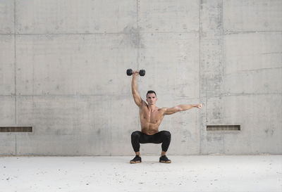 Full length of shirtless man standing against wall