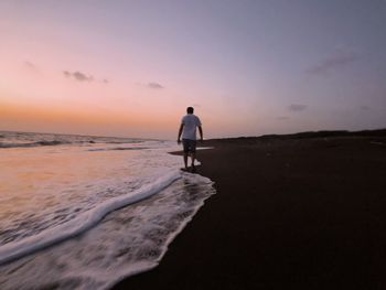 Rear view of man on beach against sky during sunset
