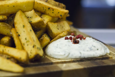Fried french fries with oregano and garlic white sauce served on a wooden board