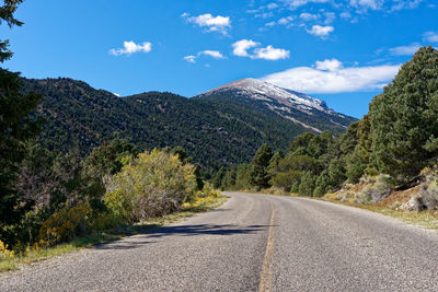 Road amidst trees and mountains against sky